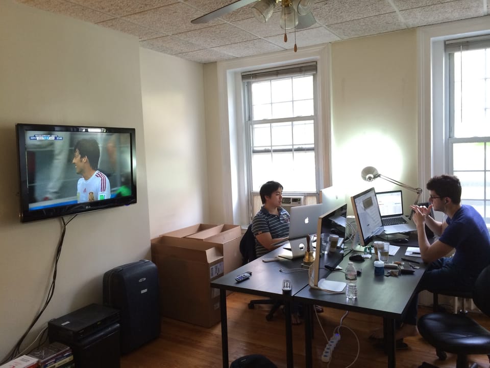 Small team working together in office with soccer match on television