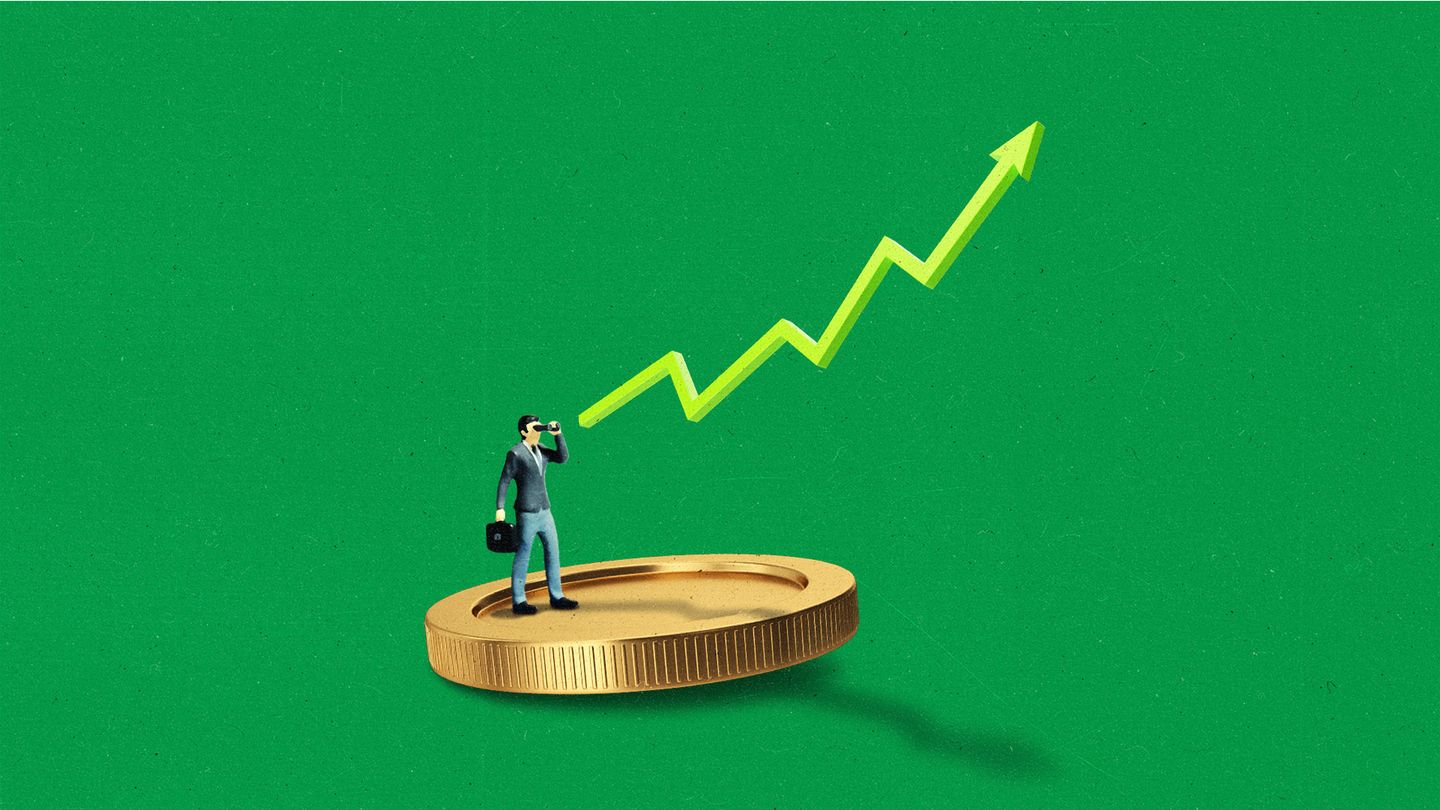 A miniature business person standing on a large coin, pointing towards an upward-trending line.