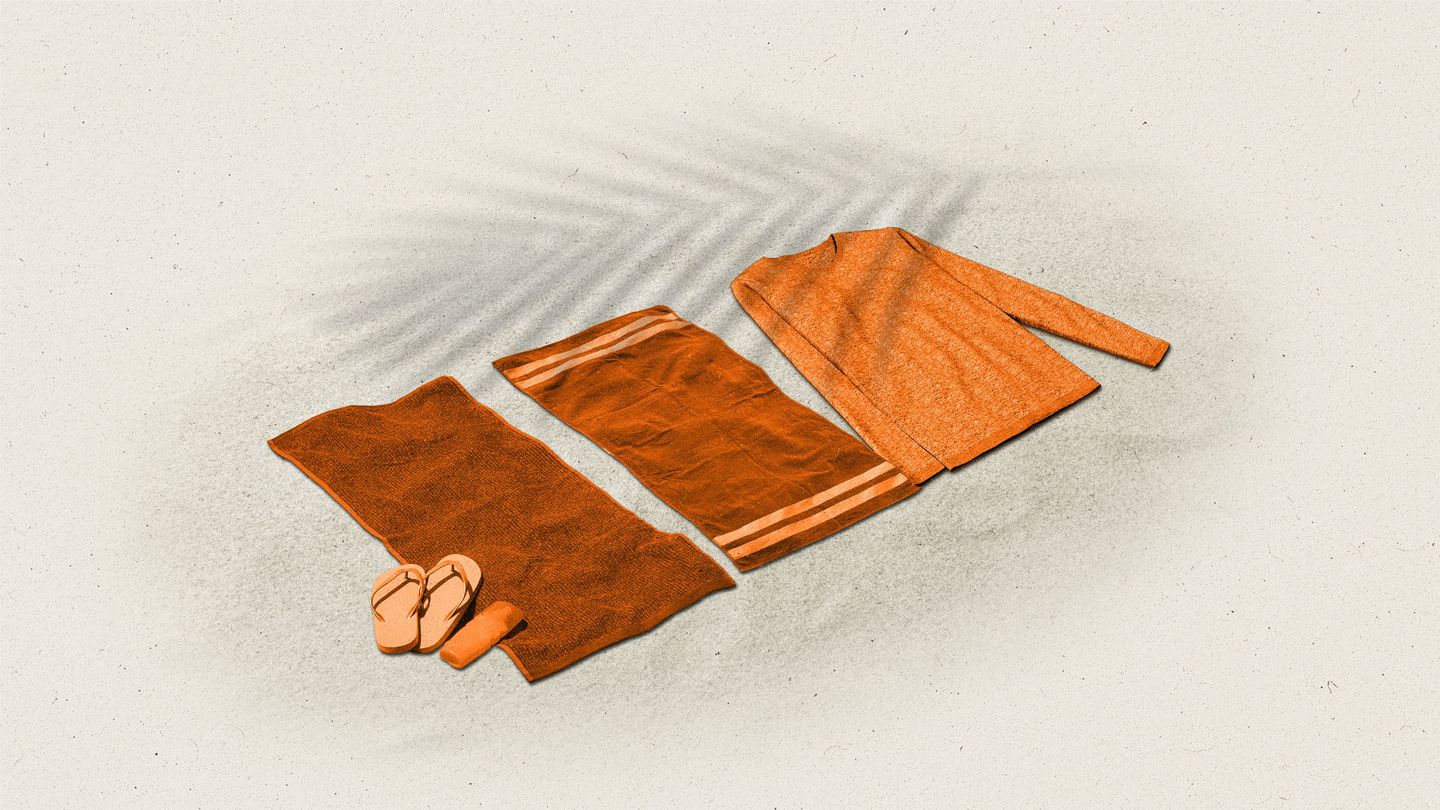Orange beach towels next to a sweater on sand with a palm tree leaf shadow.