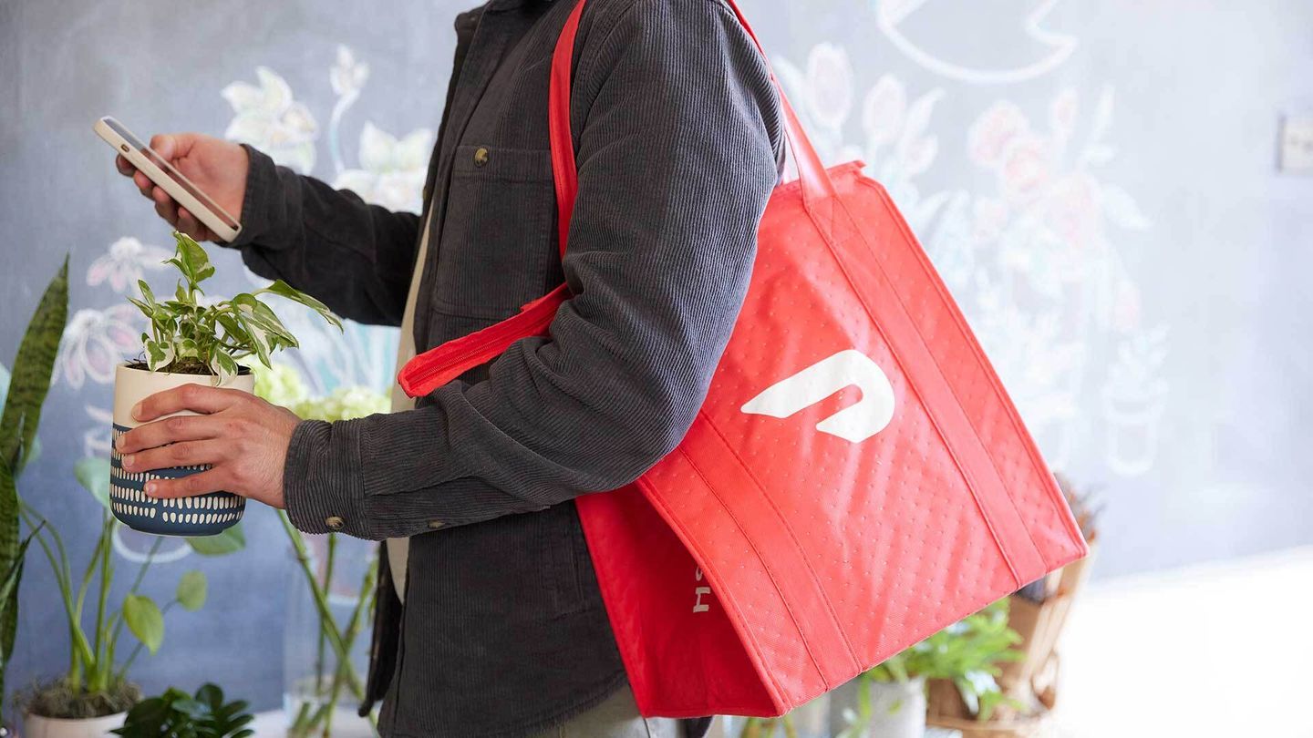 Man with a Doordash bag holds a plant and his phone.
